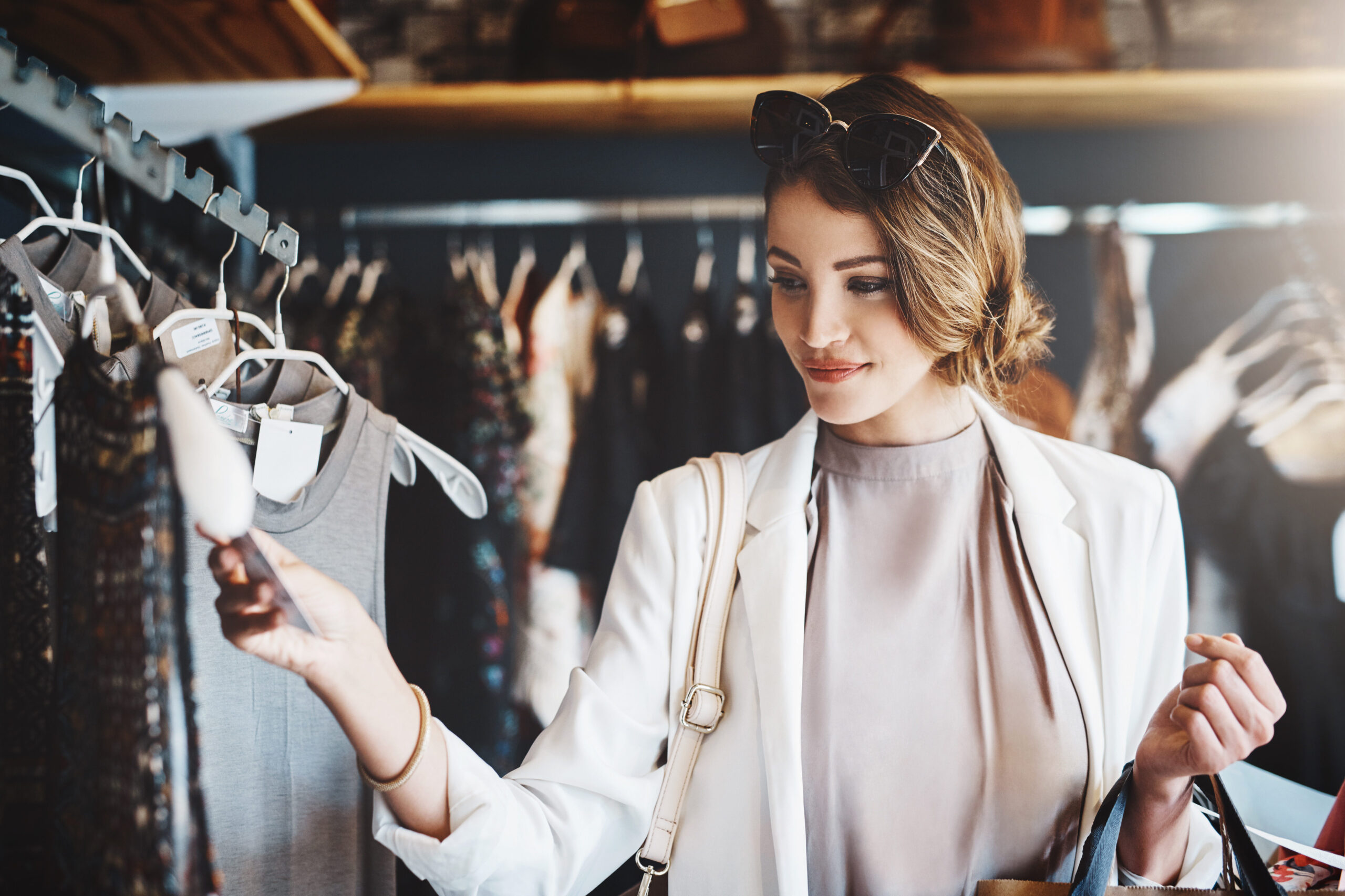 A woman shopping in a clothing store, smiling, and looking at a price tag.