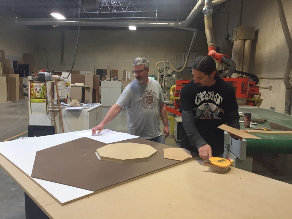 Two men are working in a shop cutting wood for retail displays.